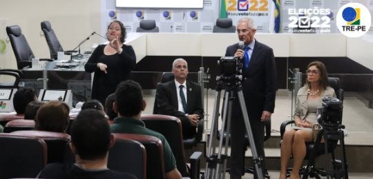 Foto do presidente do TRE-PE no Plenário do tribunal discursando para pessoas cegas e surdas, ac...